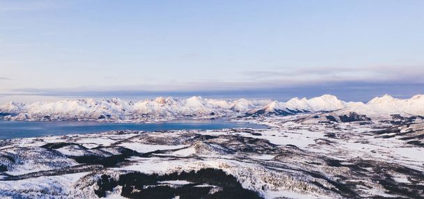 Breathtaking bird's eye view of majestic fjord mountains covered with snow in winter. Aerial view of scenery rock peaks, picturesque beautiful nature landscape. Lofoten Island surrounds by Nordic sea - Fotografie, Obrázek