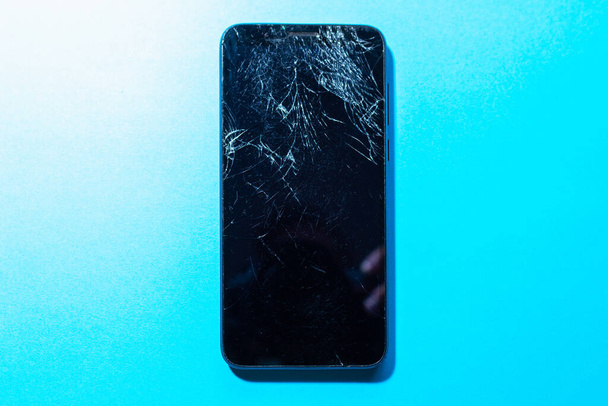 Płaski widok góry leżał Czarny rozbił smartfon z uszkodzonym ekranem i ciała na niebieskim stole w służbie. Koncepcja naprawy - Zdjęcie, obraz