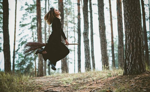 Joven mujer bruja hermosa y misteriosa Volando en el Escoba en los bosques. Levitación, una bruja con sombrero vuela sobre una escoba, espacio libre. Halloween vacaciones, magia - Foto, Imagen