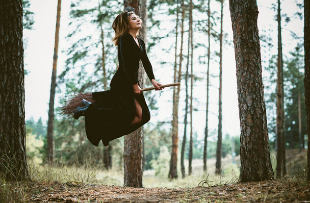 Молодая красивая и таинственная ведьма, летающая на метле в лесу. Левитация, ведьма на метле, свободное место. Хэллоуин праздник, магия - Фото, изображение