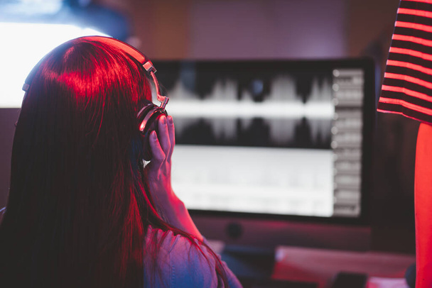 Красивая азиатская звукоинженер, работающая с цифровой звукозаписи в студии, женщина звукоинженер, глядя на форму волны на экране компьютера во время записи песни и голоса певца. - Фото, изображение