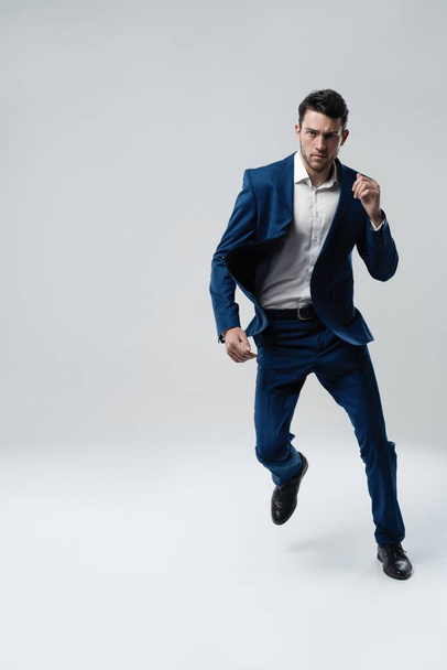 Full-length photo of funny man in suit running or jumping in air isolated over gray background. - Foto, imagen