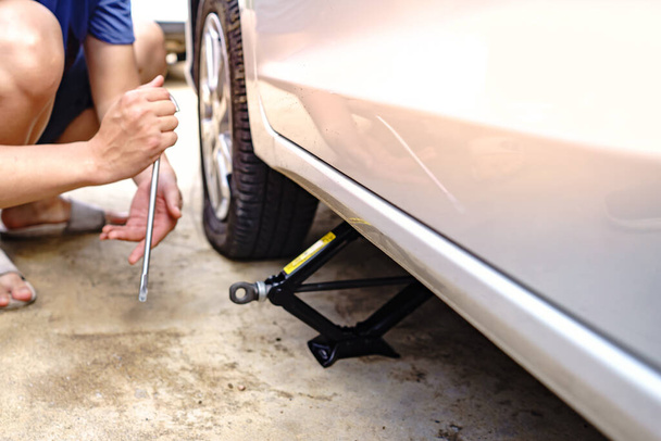 A photo of a car mechanic using a jack to change a car's wheels because the tires are broken. - Photo, Image