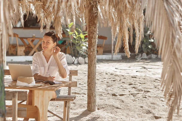 Nuori nainen käyttää kannettavaa tietokonetta rannalla. Freelance-työn käsite - Valokuva, kuva