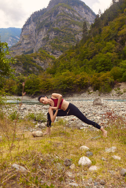 Yoga classes in nature. A woman does yoga in the mountains, near a mountain river flows. The concept of playing sports alone. Social exclusion - Photo, Image