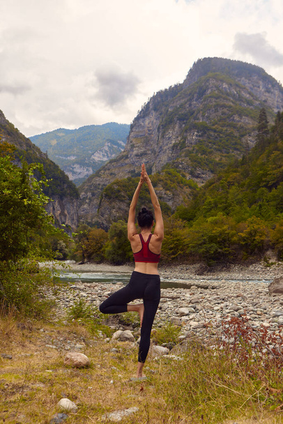 Yoga classes in nature. A woman does yoga in the mountains, near a mountain river flows. The concept of playing sports alone. Social exclusion - Photo, Image