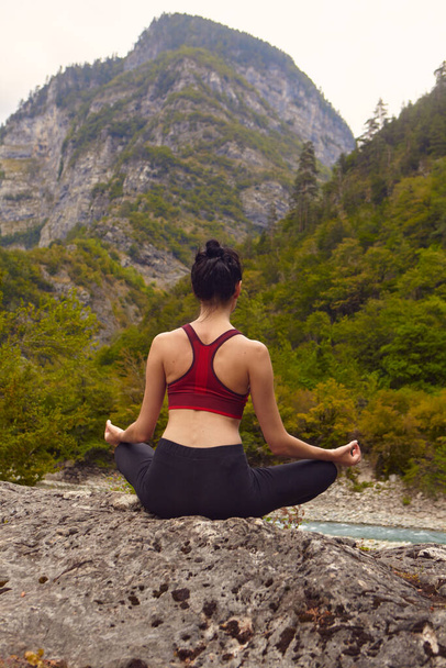Lezioni di yoga in natura. Il concetto di fare sport da solo. Esclusione sociale. Una donna fa yoga sulle rocce, vicino a un fiume di montagna scorre - Foto, immagini
