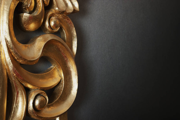 Part of golden stucco decoration in curve shape against dark wall with copy space - Foto, Imagen