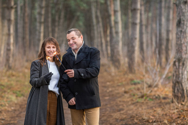Przystojny mężczyzna i kobieta w ciepłych ubraniach wyciągających dłonie z palącymi się iskrami na rozmytym tle lasu jesienią - Zdjęcie, obraz