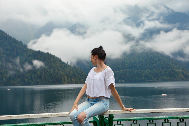 Une fille vêtue de blanc sur un fond de lac de montagne avec de l'eau bleue et des montagnes avec des nuages. Contexte. - Photo, image