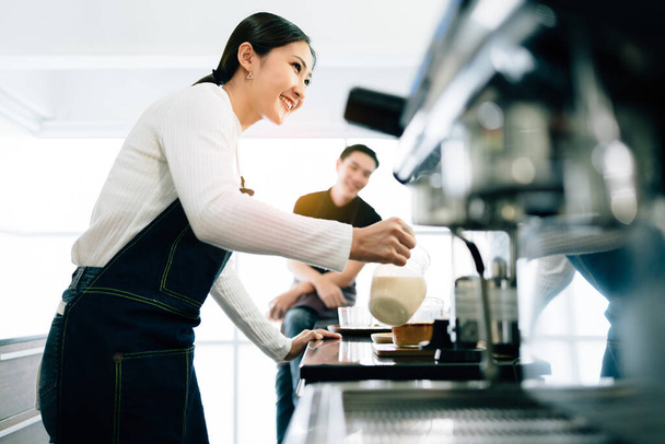A female barista student attentively measured and added milk in the coffee while the teacher watching her in the coffee shop. Coffee making classes for entrepreneurs to start small businesses. - Photo, Image