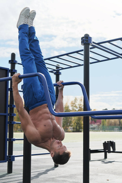 Active toned man workout on parallel bars outdoors. Active lifestyle. Muscle strength training. Open air sports ground. Phisical activity in middle age. Shirtless sportsman.  - Foto, immagini