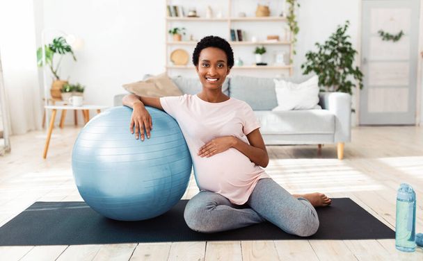 Упражнения во время беременности. Портрет счастливой будущей женщины, сидящей на коврике для йоги с мячом для фитнеса - Фото, изображение