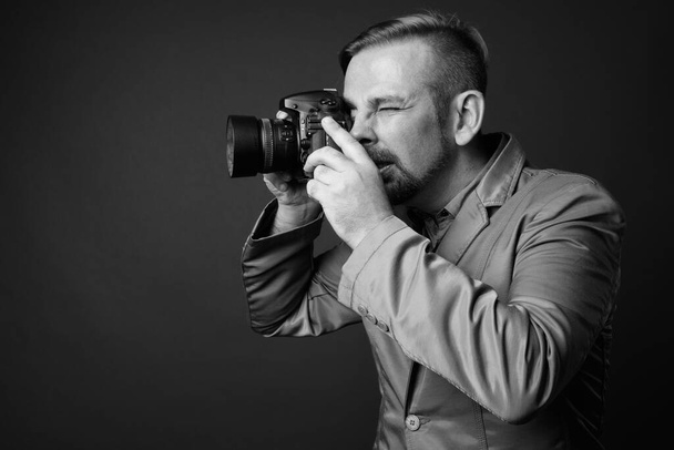 Στούντιο πλάνο του ξανθού γενειοφόρος επιχειρηματίας με μουσάκι σε γκρι φόντο σε μαύρο και άσπρο - Φωτογραφία, εικόνα