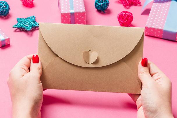 Visão superior da mulher segurando um envelope no fundo rosa feito de decorações de férias. Conceito de tempo de Natal. - Foto, Imagem