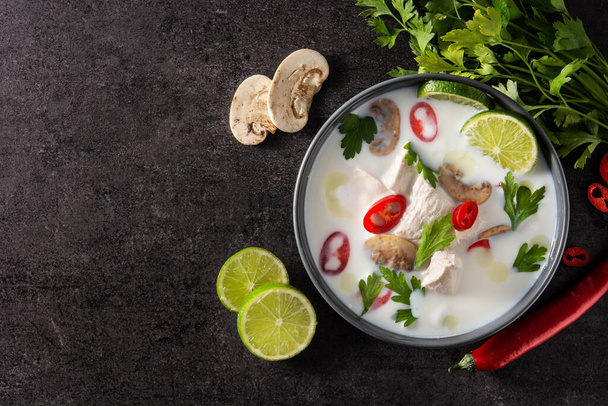 Traditional Thai food Tom Kha Gai coconut milk soup with chicken, ginger, chilli peppers,lime, and mushroom on black background - Foto, afbeelding
