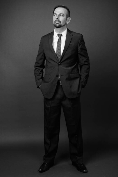 Studioaufnahme eines blonden bärtigen Geschäftsmannes mit Spitzbart vor grauem Hintergrund in Schwarz-Weiß - Foto, Bild