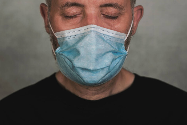 Koronawirus, zbliżenie człowieka z maską medyczną z zamkniętymi oczami na szarym tle - Zdjęcie, obraz