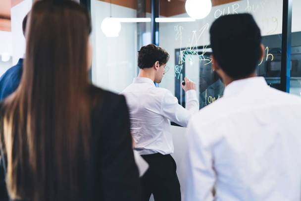 Back view of group of successful business people in formal suits standing in modern office and working on business project together - Фото, зображення