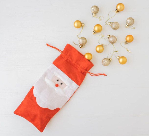 白い木製の背景に黄色と金のクリスマスのおもちゃとサンタクロースの赤いバッグ。クリスマスのコンセプト. - 写真・画像