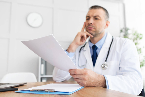 Portret dojrzałego lekarza czytającego raport medyczny - Zdjęcie, obraz