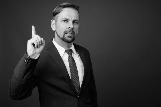 Studio shot of blond bearded businessman with goatee against gray background in black and white - Photo, Image