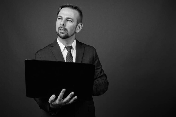 Στούντιο πλάνο του ξανθού γενειοφόρος επιχειρηματίας με μουσάκι σε γκρι φόντο σε μαύρο και άσπρο - Φωτογραφία, εικόνα