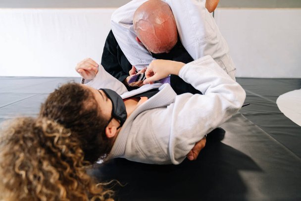 Mies ja nainen harjoittelevat kamppailulajeja ja judoa kimonojen kanssa kuntosalin lattiamatossa kasvonaamiolla 19-koronaviruspandemian vuoksi. - Valokuva, kuva