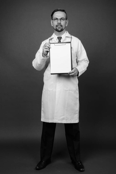 Studio shot de blond barbu homme médecin avec bouc sur fond gris en noir et blanc - Photo, image
