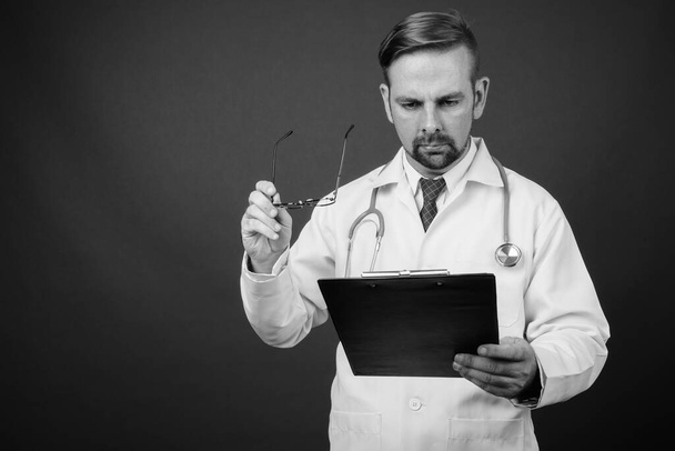 Studio záběr blond vousatý muž lékař s kozí bradkou proti šedému pozadí v černé a bílé - Fotografie, Obrázek