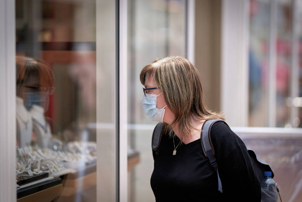  Женщина ходит по магазинам с защитной маской из-за существующих требований к маске                               - Фото, изображение