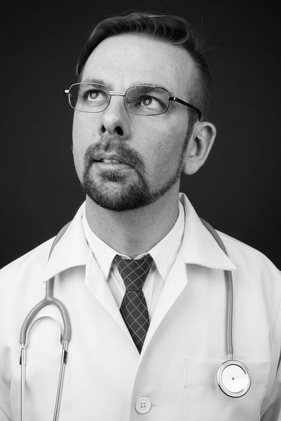 Estudio de hombre barbudo rubio médico con perilla sobre fondo gris en blanco y negro - Foto, Imagen