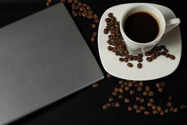 Ένα φλιτζάνι καφέ δίπλα σε ταμπλέτα και κόκκους καφέ. - Φωτογραφία, εικόνα