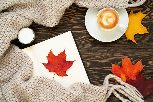 Cozy and warm autumn flat lay with cup of coffee, open book, candle, knitted plaid, red, orange and yellow leaves on wooden background.  - Foto, immagini