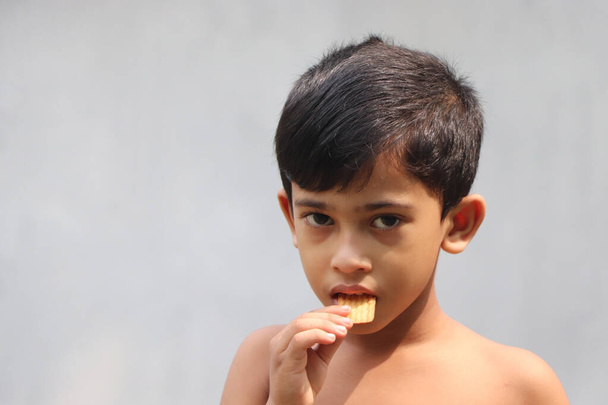 Aranyos kisfiú, aki kekszet eszik. Sült és feldolgozott élelmiszer koncepció elszigetelt másolási tér szürke háttér - Fotó, kép