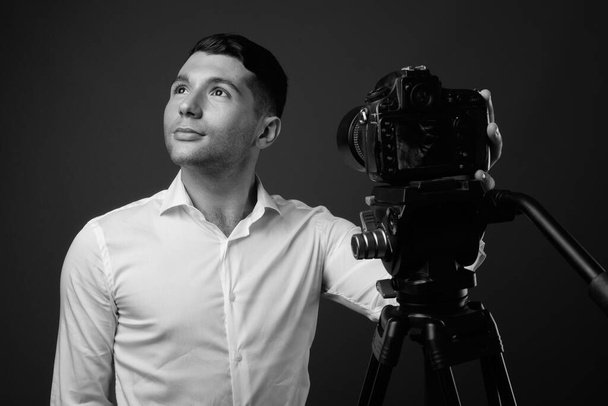 Studio shot of young handsome businessman vlogging against gray background in black and white - Photo, Image