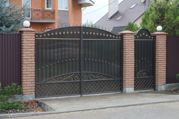 portões de metal preto um padrão forjado e parte de uma cerca marrom tijolo na rua - Foto, Imagem