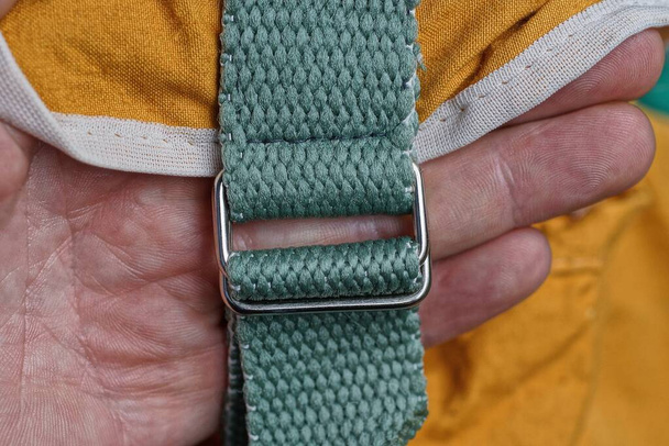 hand holds a green harness with metal clasp on the brown fabric of the backpack - Photo, Image