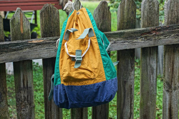 one colored backpack hanging on gray wooden fence boards in the street - Photo, Image