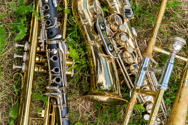 Musical instruments including trombone trumpet clarinet and saxophone lay in grassy field at music festival - Photo, Image