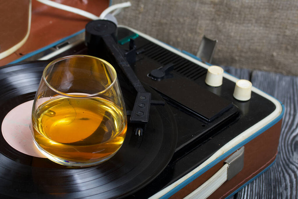 Old turntable. Nearby is a glass of strong alcohol. Retro party equipment. - Foto, Bild