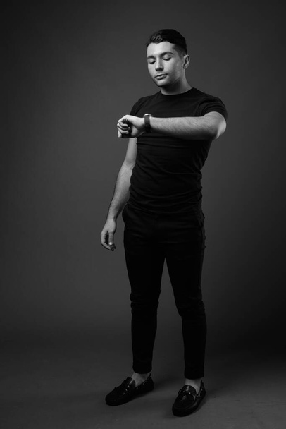 Studio shot of young handsome man against gray background in black and white - Fotó, kép