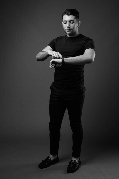 Studio záběr mladého pohledného muže proti šedé pozadí v černé a bílé - Fotografie, Obrázek
