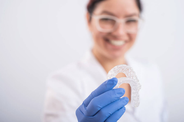 Smiling female orthodontist holds two transparent aligners. The dentist demonstrates the bite correction device - Foto, Bild