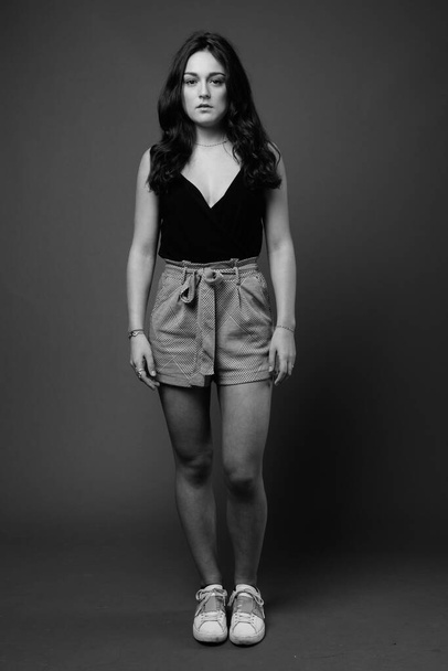 Studio shot of young beautiful woman wearing black sleeveless top against gray background in black and white - Photo, Image