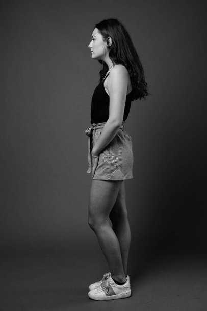 Στούντιο πλάνο της νεαρής όμορφης γυναίκας φορώντας μαύρο αμάνικο τοπ σε γκρι φόντο σε μαύρο και άσπρο - Φωτογραφία, εικόνα