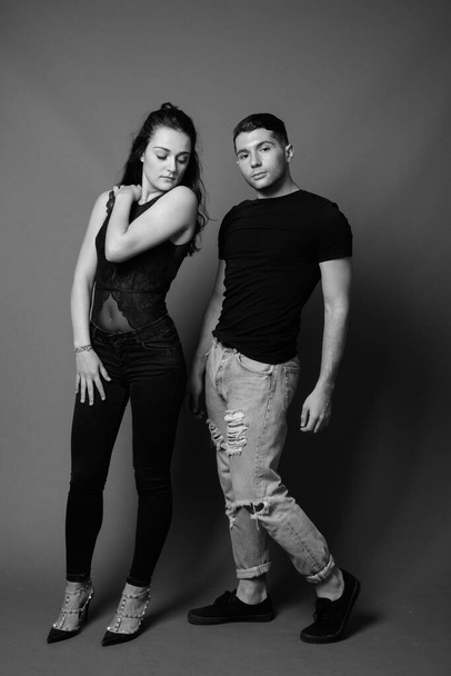 Στούντιο πλάνο του νεαρού ζευγαριού μαζί και ερωτευμένος με γκρι φόντο σε μαύρο και άσπρο - Φωτογραφία, εικόνα