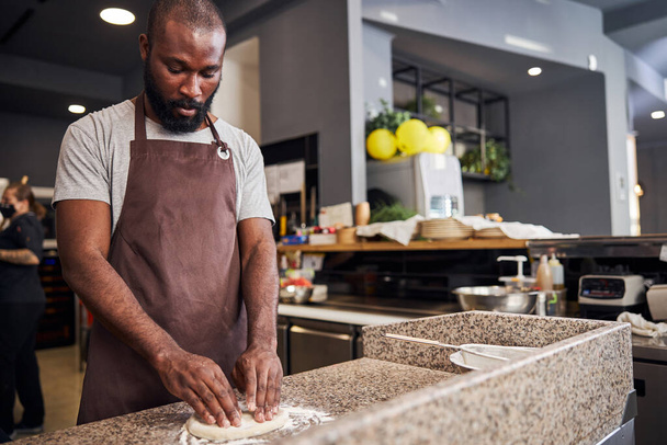 Handsome cooker preparing dough in restaurant kitchen - Фото, изображение