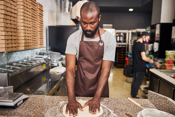 Young bearded man making pizza in kitchen - 写真・画像