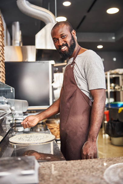 Cheerful young cooker making pizza in restaurant - Foto, imagen